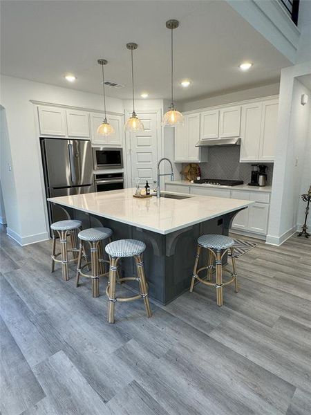 Kitchen featuring sink, white cabinets, hanging light fixtures, and stainless steel appliances