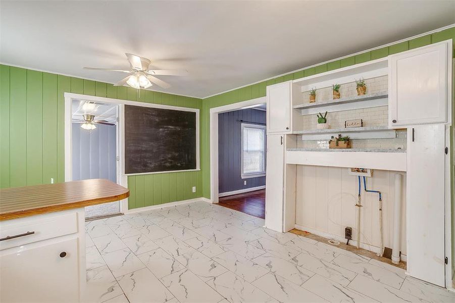 Kitchen featuring ceiling fan, crown molding, wooden walls, and white cabinets