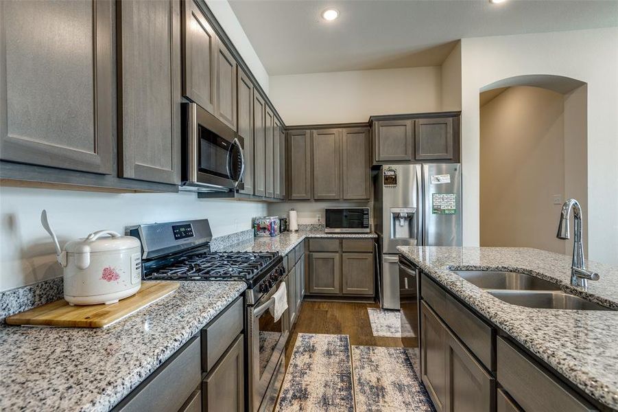 Kitchen with appliances with stainless steel finishes, light stone countertops, sink, and dark wood-type flooring