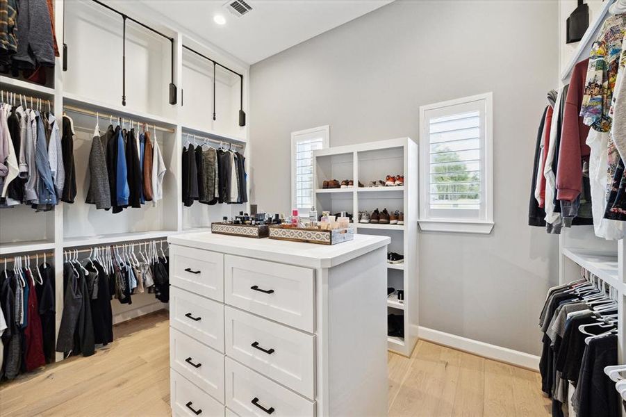 Primary closet with with engineered wood floors, recessed lighting, and plantation shutters.
