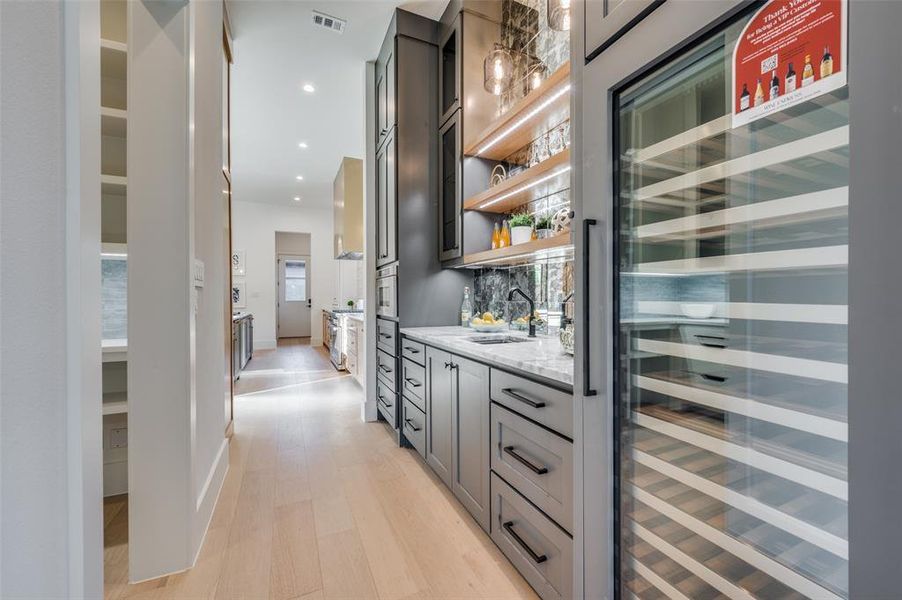 Bar featuring gray cabinetry, beverage cooler, light hardwood / wood-style flooring, light stone counters, and decorative backsplash