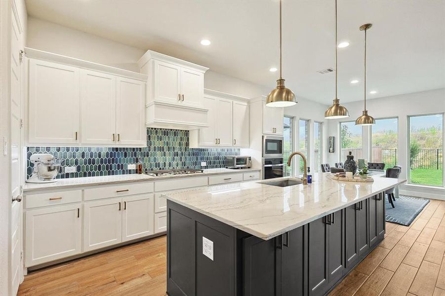 Kitchen featuring premium range hood, light hardwood / wood-style floors, a kitchen island with sink, hanging light fixtures, and white cabinets