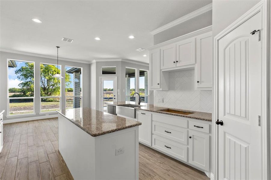 Kitchen with light hardwood / wood-style floors, white cabinets, dark stone countertops, and a wealth of natural light