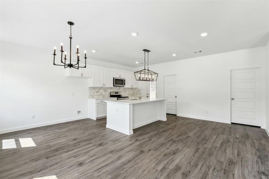 Kitchen featuring a center island with sink, dark wood-type flooring, hanging light fixtures, white cabinets, and appliances with stainless steel finishes