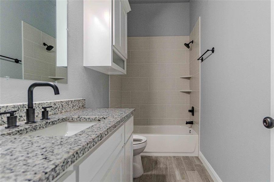 Full bathroom featuring hardwood / wood-style floors, vanity, toilet, and tiled shower / bath combo