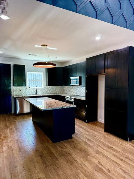 Kitchen with light hardwood / wood-style flooring, a center island, decorative light fixtures, and stainless steel appliances