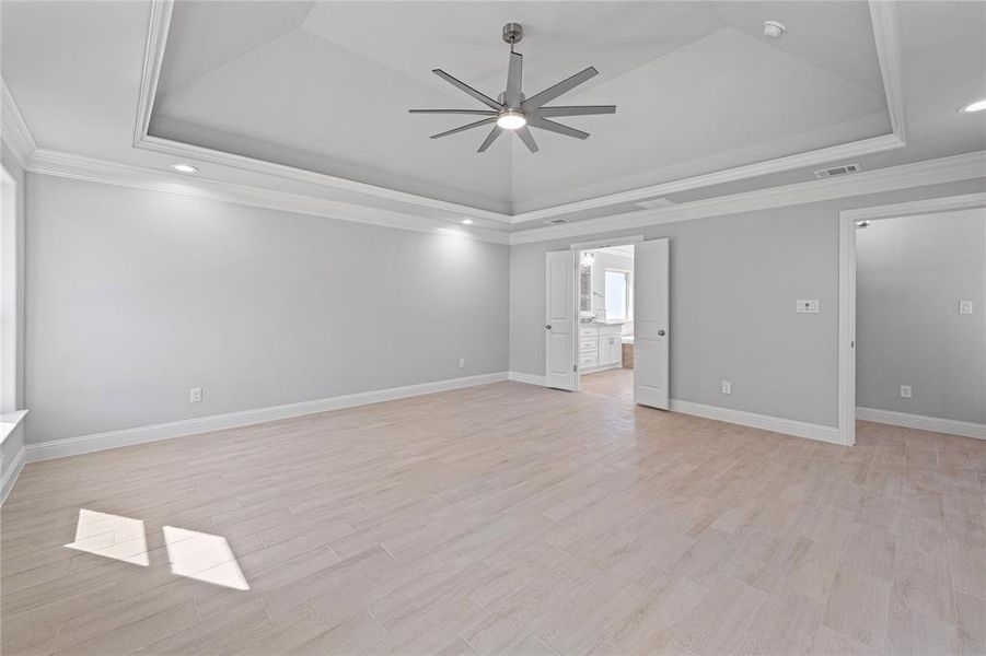 Spare room with ceiling fan, crown molding, a tray ceiling, and light hardwood / wood-style floors