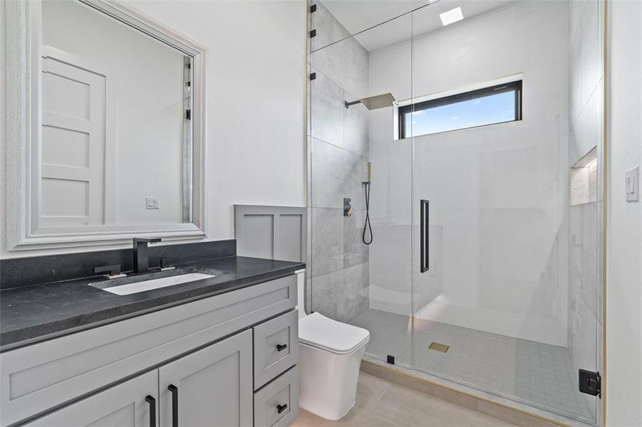 Bathroom with a shower with shower door, vanity with extensive cabinet space, tile flooring, and toilet