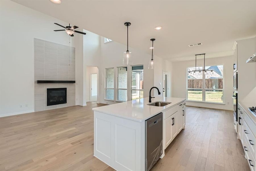 Kitchen featuring an island with sink, stainless steel appliances, sink, a tile fireplace, and decorative light fixtures