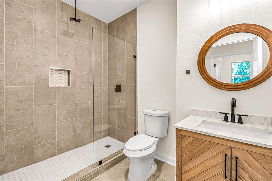 Guest bath also features stained wood vanity and seamless glass enclosure.