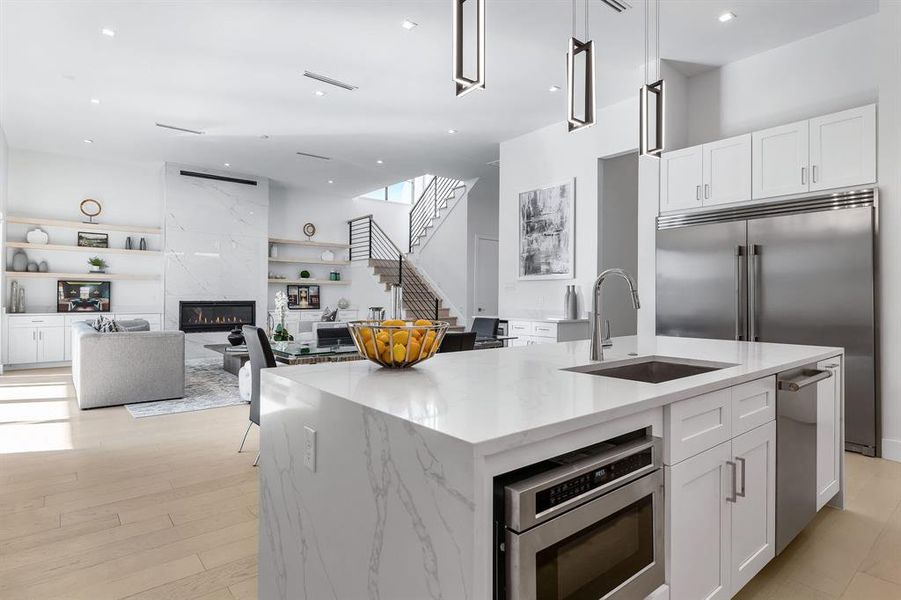 Kitchen with a high end fireplace, appliances with stainless steel finishes, an island with sink, sink, and white cabinetry