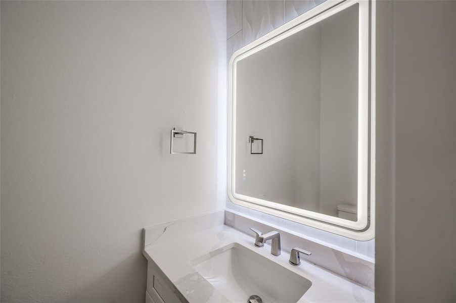 The powder room on the second floor features a tile accent wall and contemporary backlit mirror.