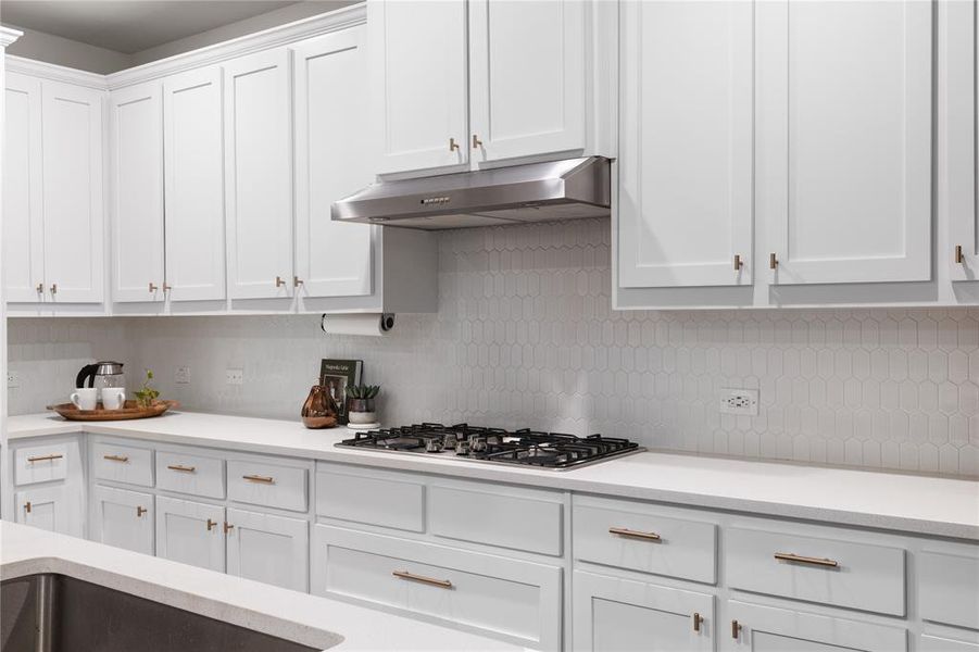 Kitchen featuring stainless steel gas stovetop, backsplash, and white cabinets