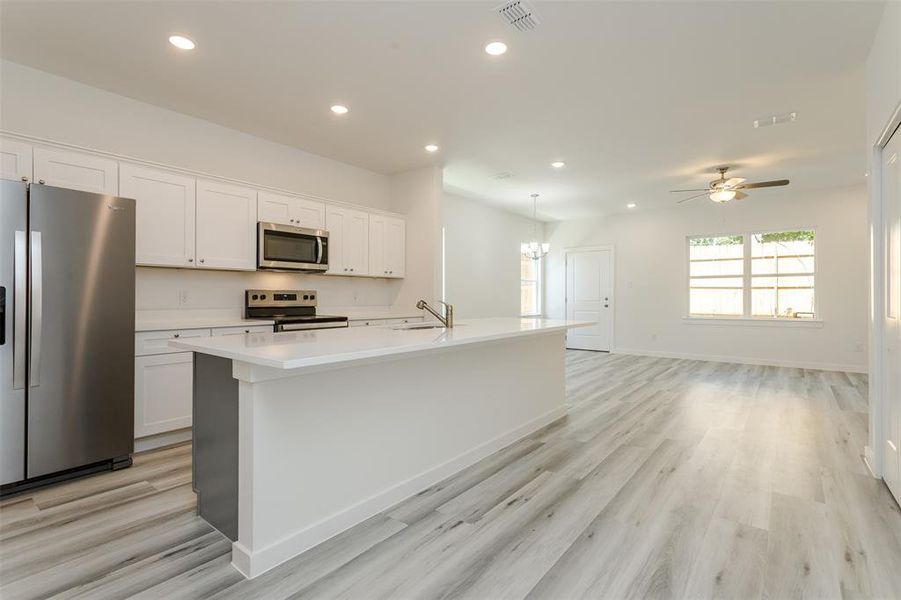 Kitchen featuring appliances with stainless steel finishes, white cabinets, light wood-type flooring, and an island with sink