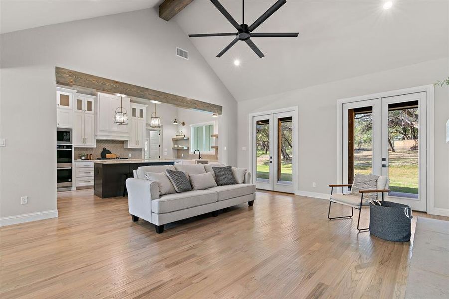 Living room with french doors, beamed ceiling, high vaulted ceiling, light hardwood / wood-style floors, and ceiling fan