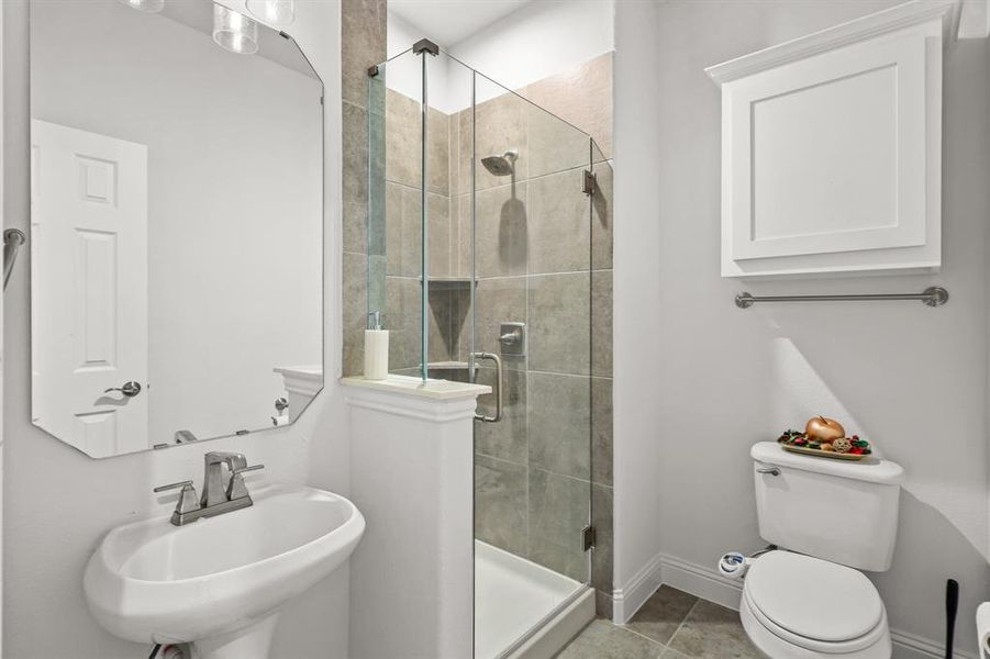 Bathroom with sink, a shower with door, tile patterned floors, and toilet