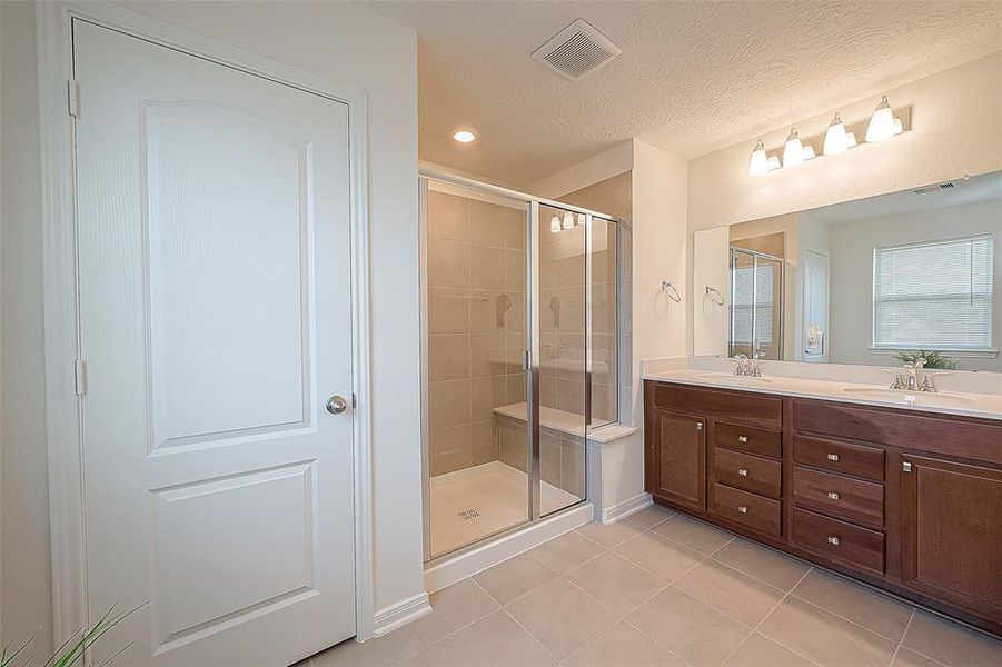 Primary bathroom with extra linen closet, double sinks, and expansive shower with seat