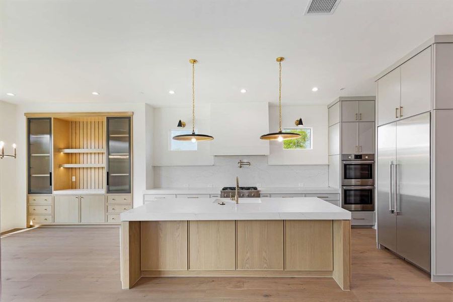 Kitchen featuring pendant lighting, light wood-type flooring, tasteful backsplash, a center island with sink, and appliances with stainless steel finishes