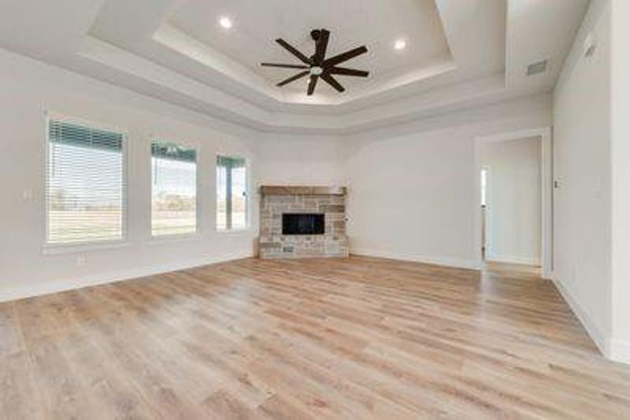 Unfurnished living room featuring a stone fireplace, ceiling fan, light wood-type flooring, and a raised ceiling