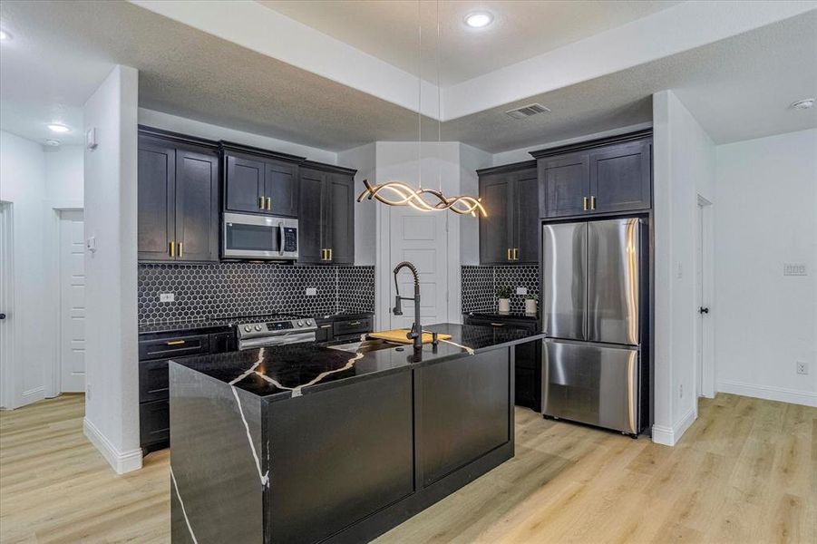 Kitchen featuring light hardwood / wood-style flooring, a center island with sink, tasteful backsplash, appliances with stainless steel finishes, and sink