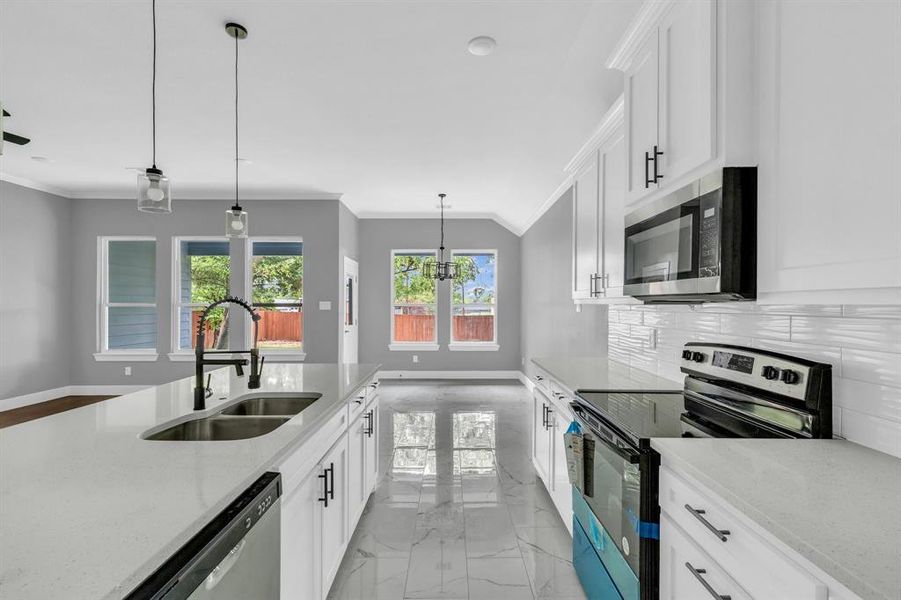 Kitchen with light stone counters, white cabinets, stainless steel appliances, and sink