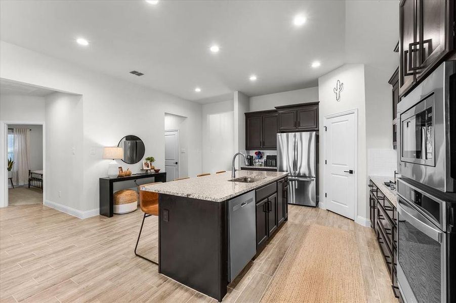 Kitchen with sink, light wood-type flooring, an island with sink, appliances with stainless steel finishes, and light stone counters