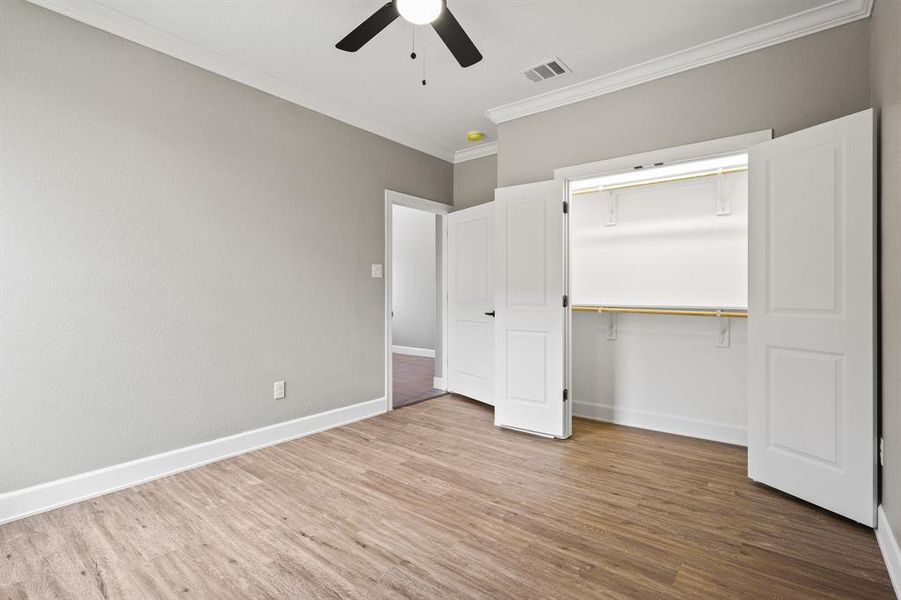 Unfurnished bedroom with ornamental molding, a closet, ceiling fan, and hardwood / wood-style floors