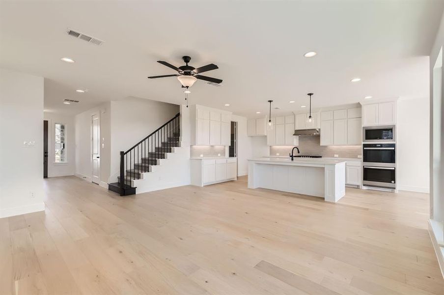 Kitchen featuring white cabinets, a center island with sink, light wood-type flooring, decorative light fixtures, and stainless steel appliances