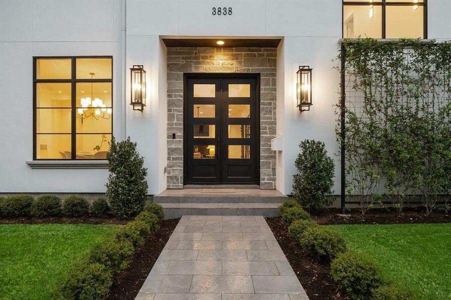 The grand entrance is highlighted by stunning contemporary sconce lanterns, and the contemporary custom black iron doors are surrounded by stone.