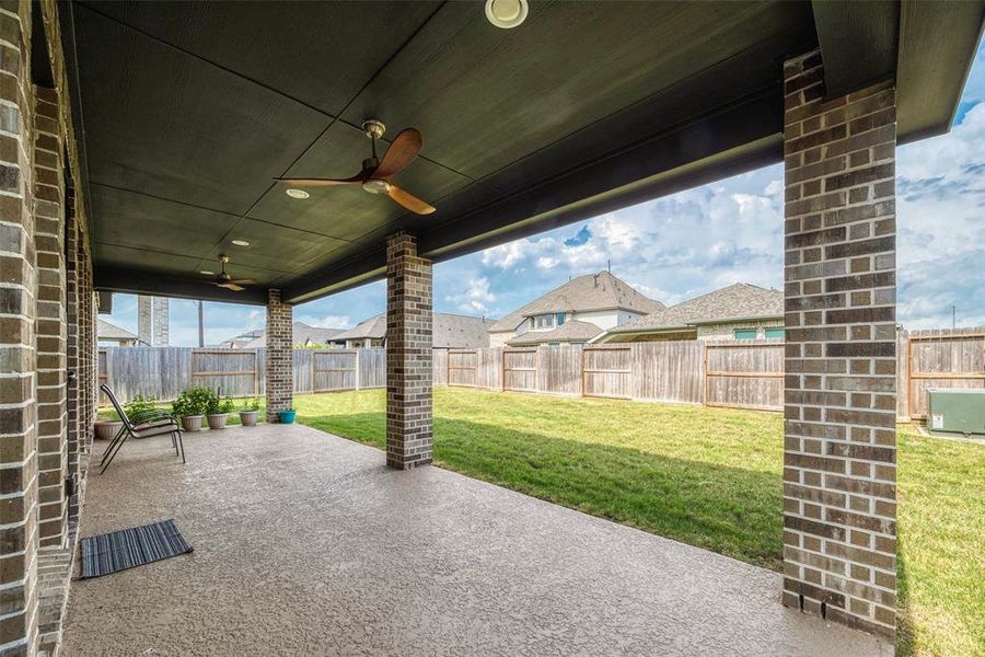 Spacious covered patio with ceiling fans, overlooking a large fenced backyard.