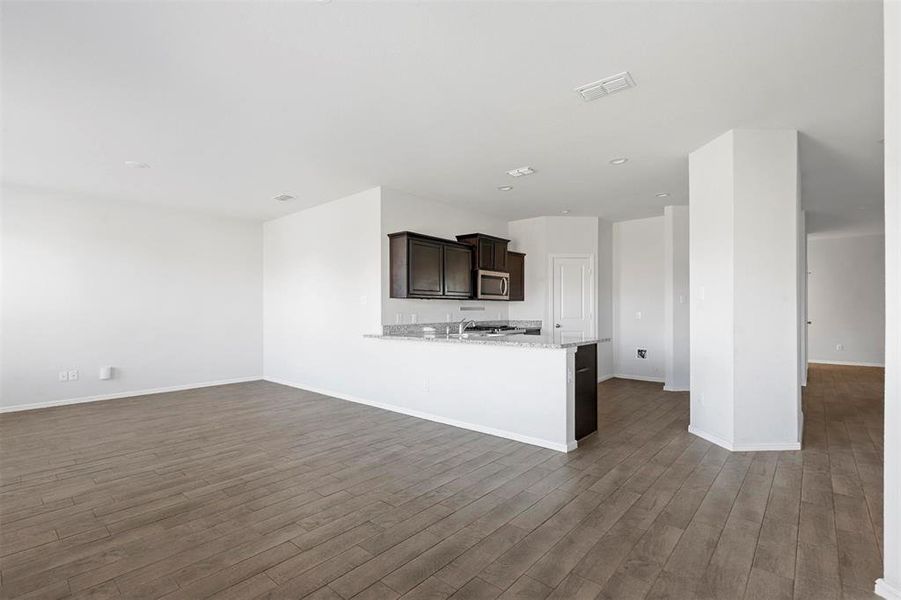 Kitchen featuring dark brown cabinets, kitchen peninsula, dark hardwood / wood-style floors, and light stone counters