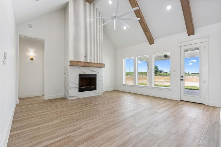 Unfurnished living room with light hardwood / wood-style floors, high vaulted ceiling, a high end fireplace, and ceiling fan