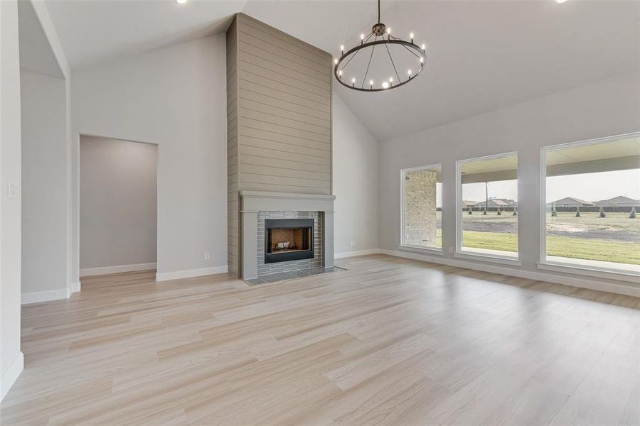 Unfurnished living room featuring an inviting chandelier, light hardwood / wood-style flooring, a tiled fireplace, and high vaulted ceiling