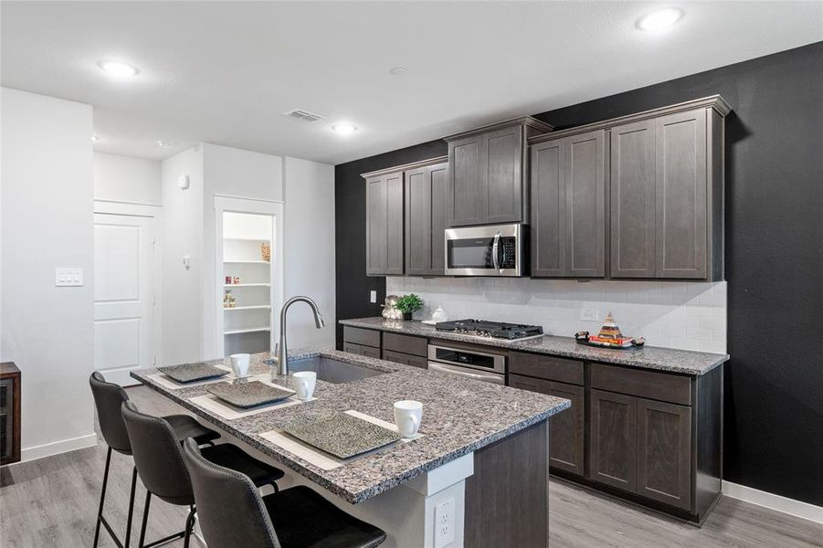 Kitchen with stainless steel appliances, a kitchen breakfast bar, sink, decorative backsplash, and a center island with sink