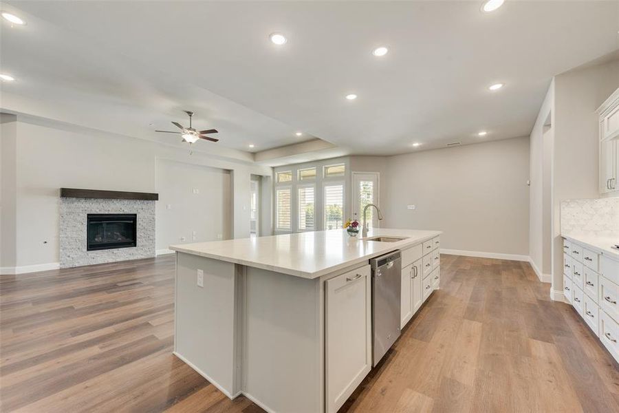 Kitchen with an island with sink, stainless steel dishwasher, white cabinetry, and light wood-type flooring