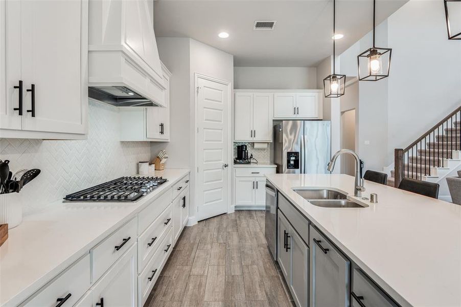 Kitchen featuring stainless steel appliances, hardwood / wood-style floors, backsplash, decorative light fixtures, and custom exhaust hood