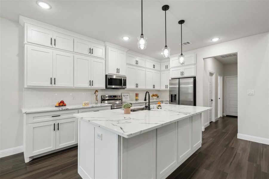 Kitchen with appliances with stainless steel finishes, dark hardwood / wood-style flooring, decorative light fixtures, and a center island with sink