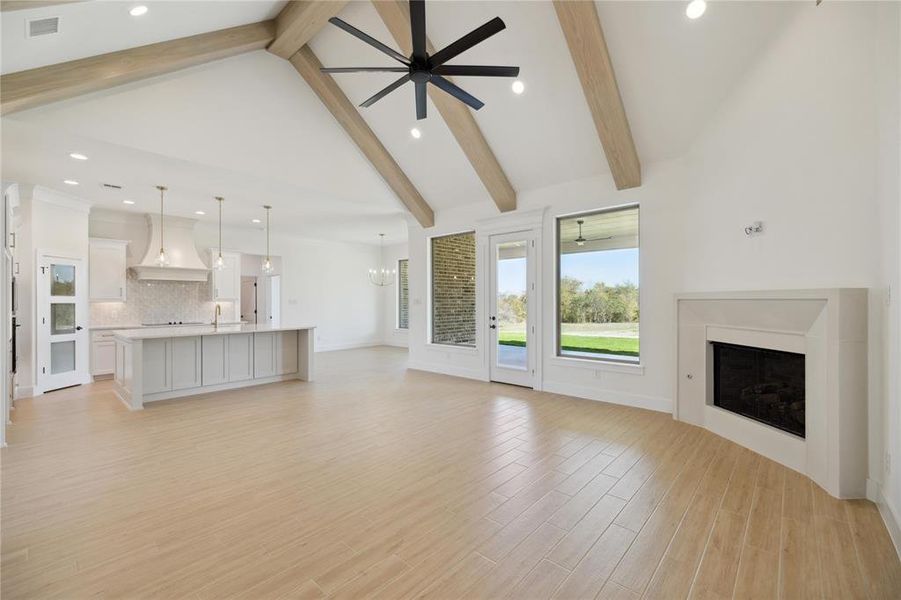 Unfurnished living room with light hardwood / wood-style floors, beamed ceiling, ceiling fan with notable chandelier, and high vaulted ceiling