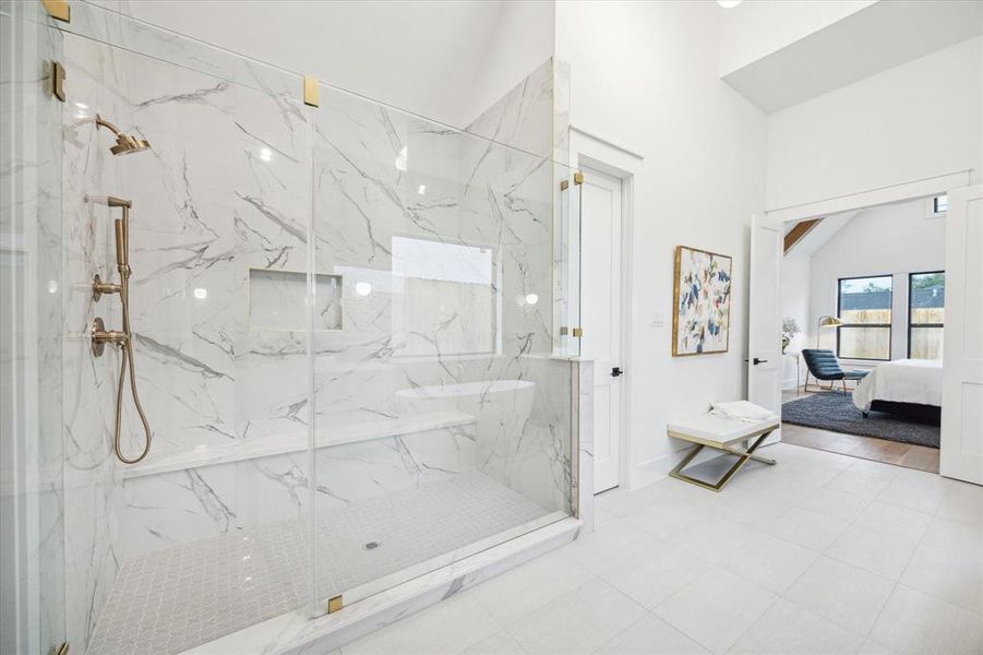 Shower in style with a frameless glass door, bench, shower head and handheld spray.  Beatiful floor to ceiling glazed porcelein shower tile with decorative veining add beauty to this functional area.