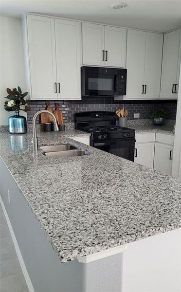 Kitchen with light stone counters, tasteful backsplash, white cabinetry, black appliances, and sink