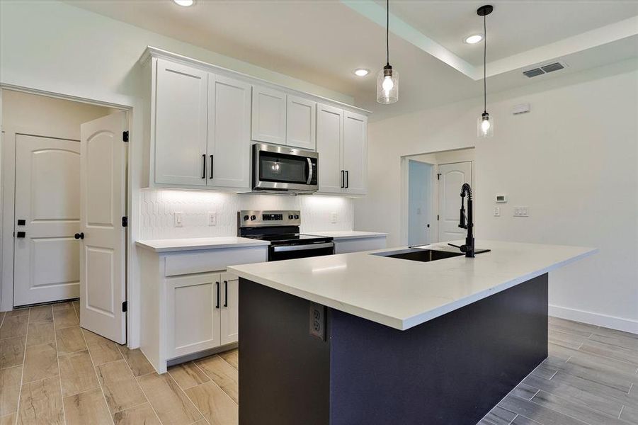 Kitchen featuring stainless steel appliances, decorative light fixtures, white cabinetry, and a kitchen island with sink