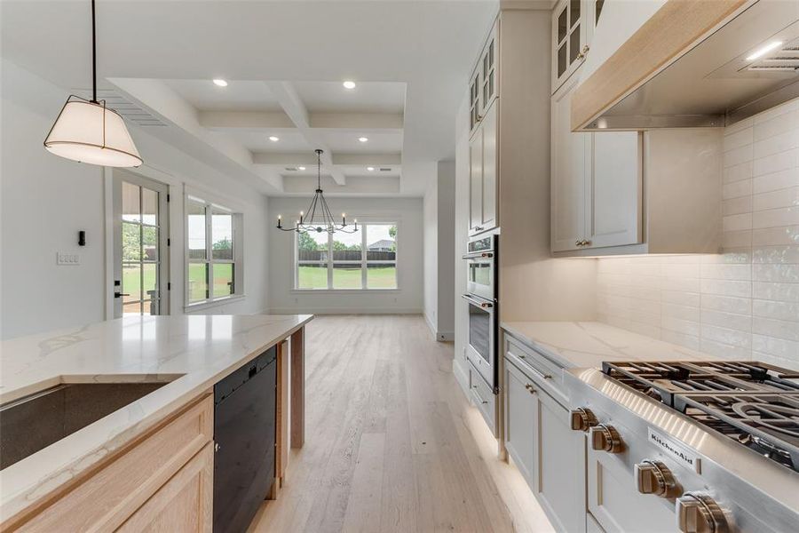 Kitchen featuring tasteful backsplash, light wood-type flooring, cooktop, custom exhaust hood, and coffered ceiling