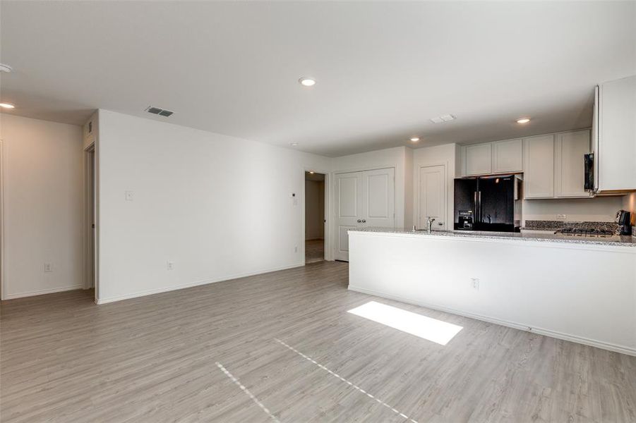 Kitchen with black fridge, light hardwood / wood-style flooring, white cabinets, and light stone countertops