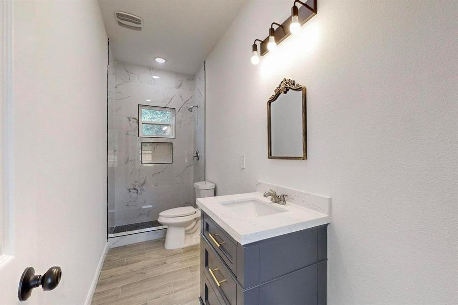 Bathroom with tiled shower, wood-type flooring, toilet, and vanity