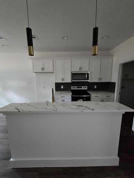 Kitchen featuring light stone counters, decorative light fixtures, white cabinetry, stainless steel appliances, and a center island