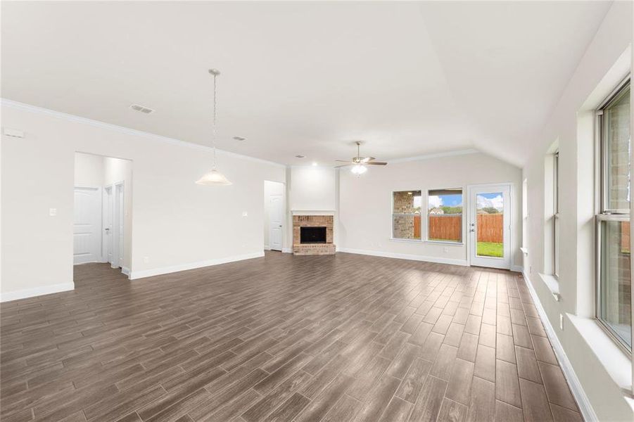 Unfurnished living room with a brick fireplace, ceiling fan, crown molding, vaulted ceiling, and dark hardwood / wood-style floors