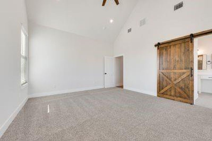 Unfurnished room featuring a barn door, light colored carpet, high vaulted ceiling, and ceiling fan