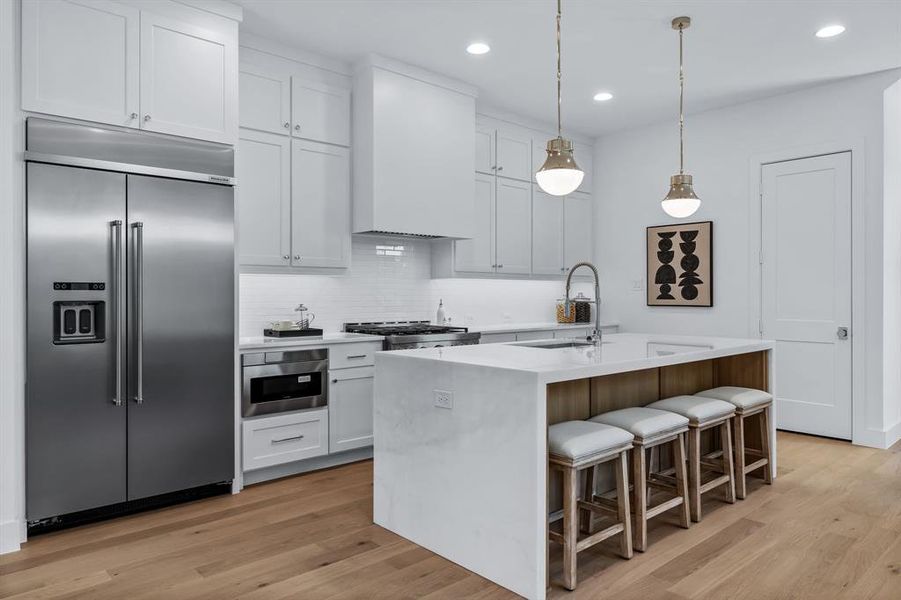 Kitchen featuring appliances with stainless steel finishes, hanging light fixtures, white cabinets, and an island with sink