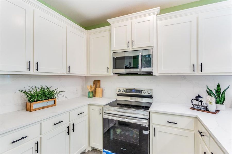 Kitchen with white cabinets, electric stove, decorative backsplash, and light stone counters