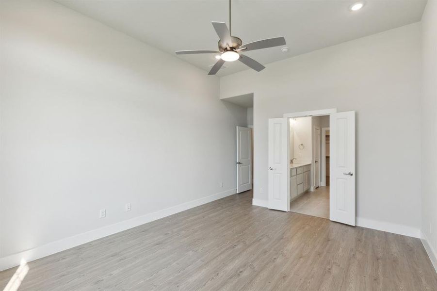 Unfurnished bedroom with ceiling fan, light wood-type flooring, and ensuite bathroom